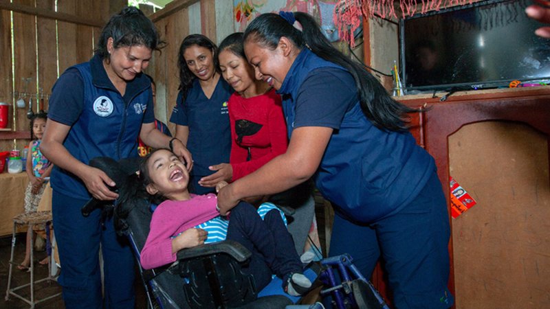 Personal de atención social acompaña a una niña durante la entrega de una silla de ruedas en su hogar. La imagen refleja la asistencia directa a personas con discapacidad y sus familias, uno de los componentes de la Misión Solidaria Manuela Espejo. Fuente: Portal de la Presidencia de la República del Ecuador.