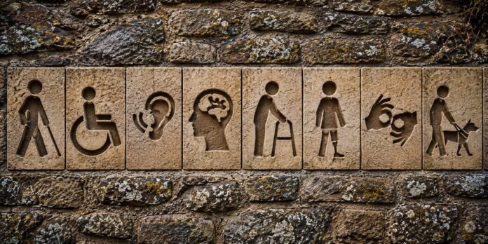 La discapacidad tiene distintas manifestaciones y requiere respuestas que garanticen la accesibilidad, la autonomía y la igualdad de oportunidades. Esta composición gráfica representa algunas de ellas mediante símbolos integrados en un muro de piedra. Imagen: Recreación digital elaborada para El Costanero a partir de una fotografía original de Gryziu, publicada en Pexels.